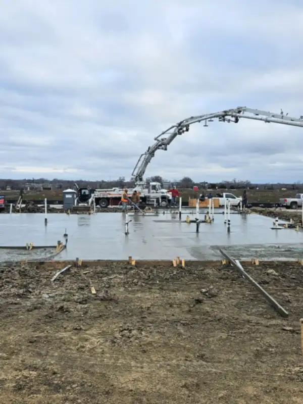Concrete pump boom placing a foundation slab beside a framed house
