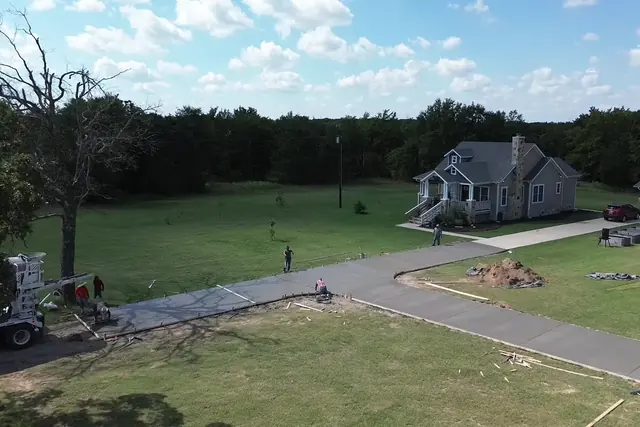 Long new concrete driveway curving up to a single-story home on a grassy lot